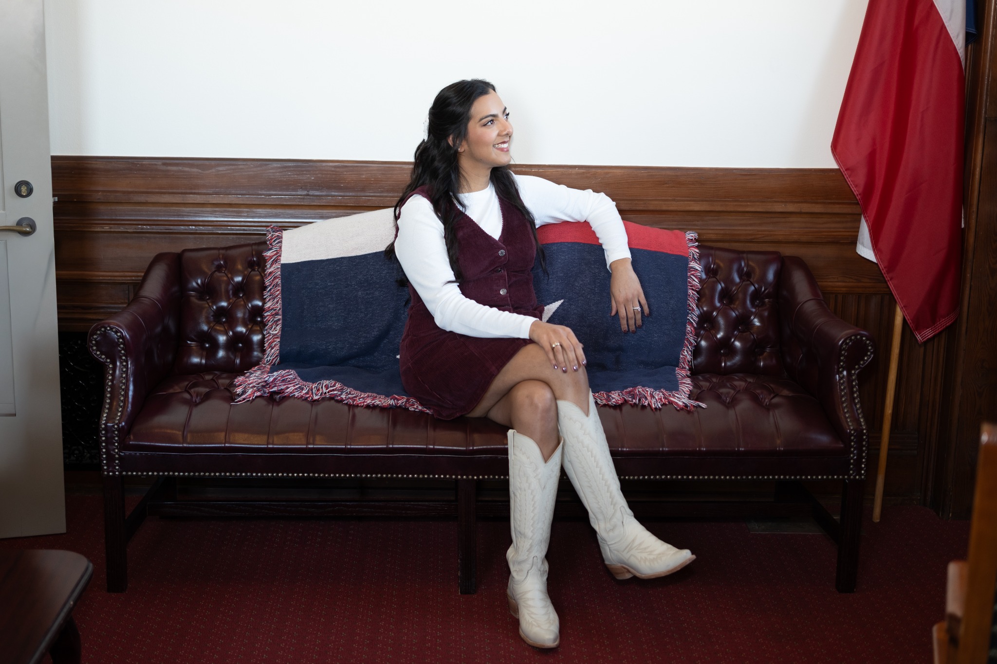 A woman in a burgundy dress and white cowboy boots seated on a leather sofa