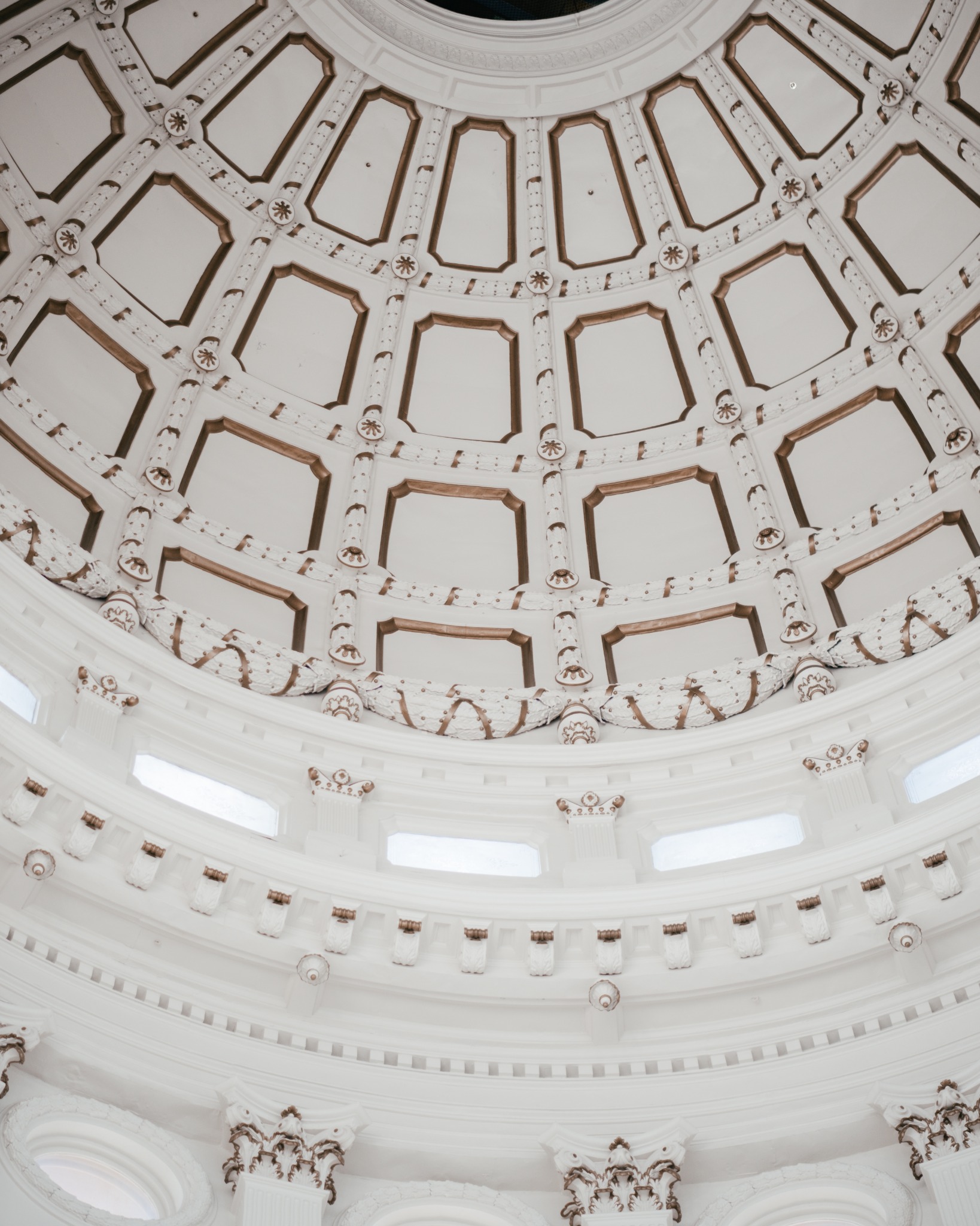 An upward view of the ornate coffered interior of a white rotunda dome