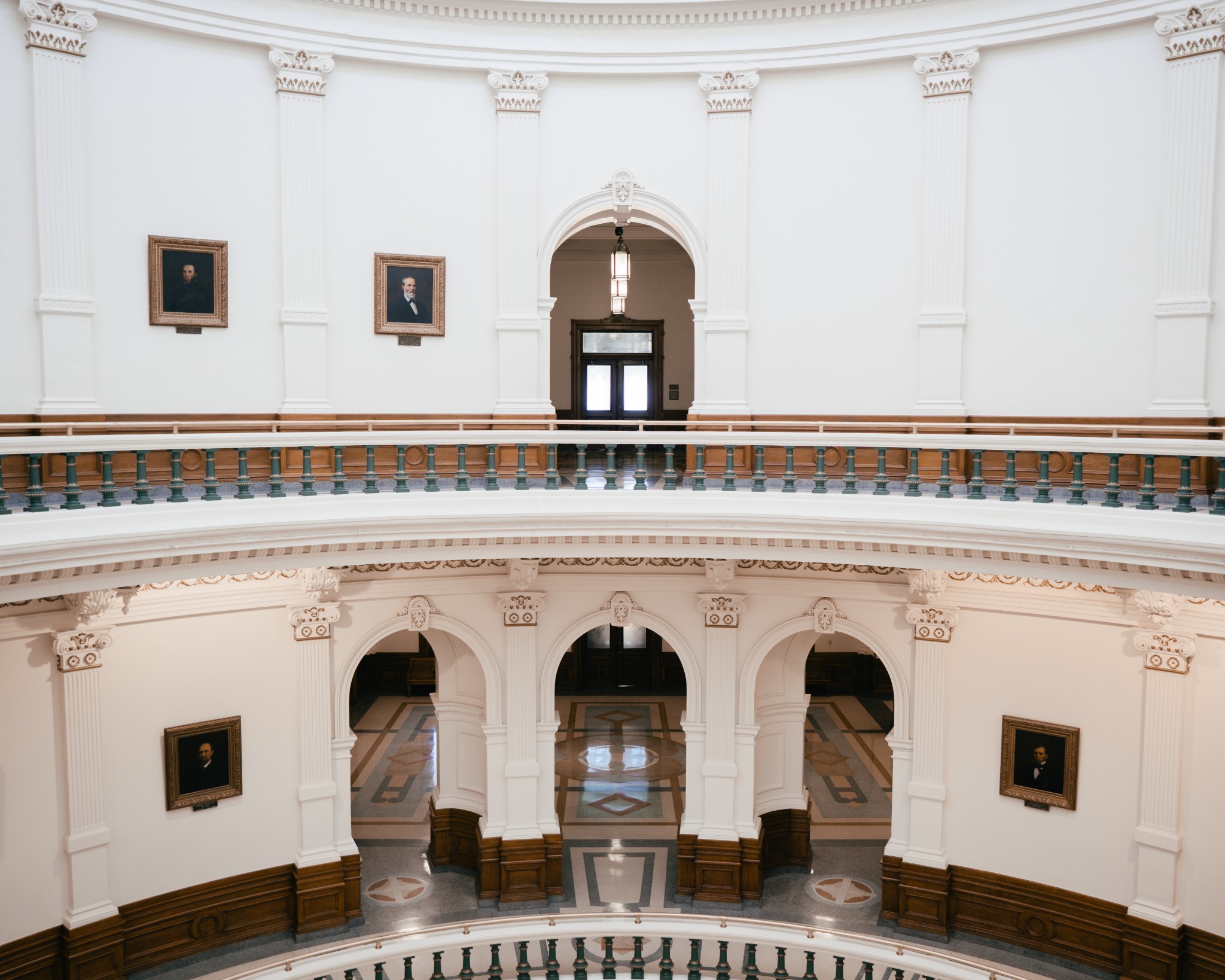 Curved balconies, framed portraits, and arched doorways inside a bright rotunda