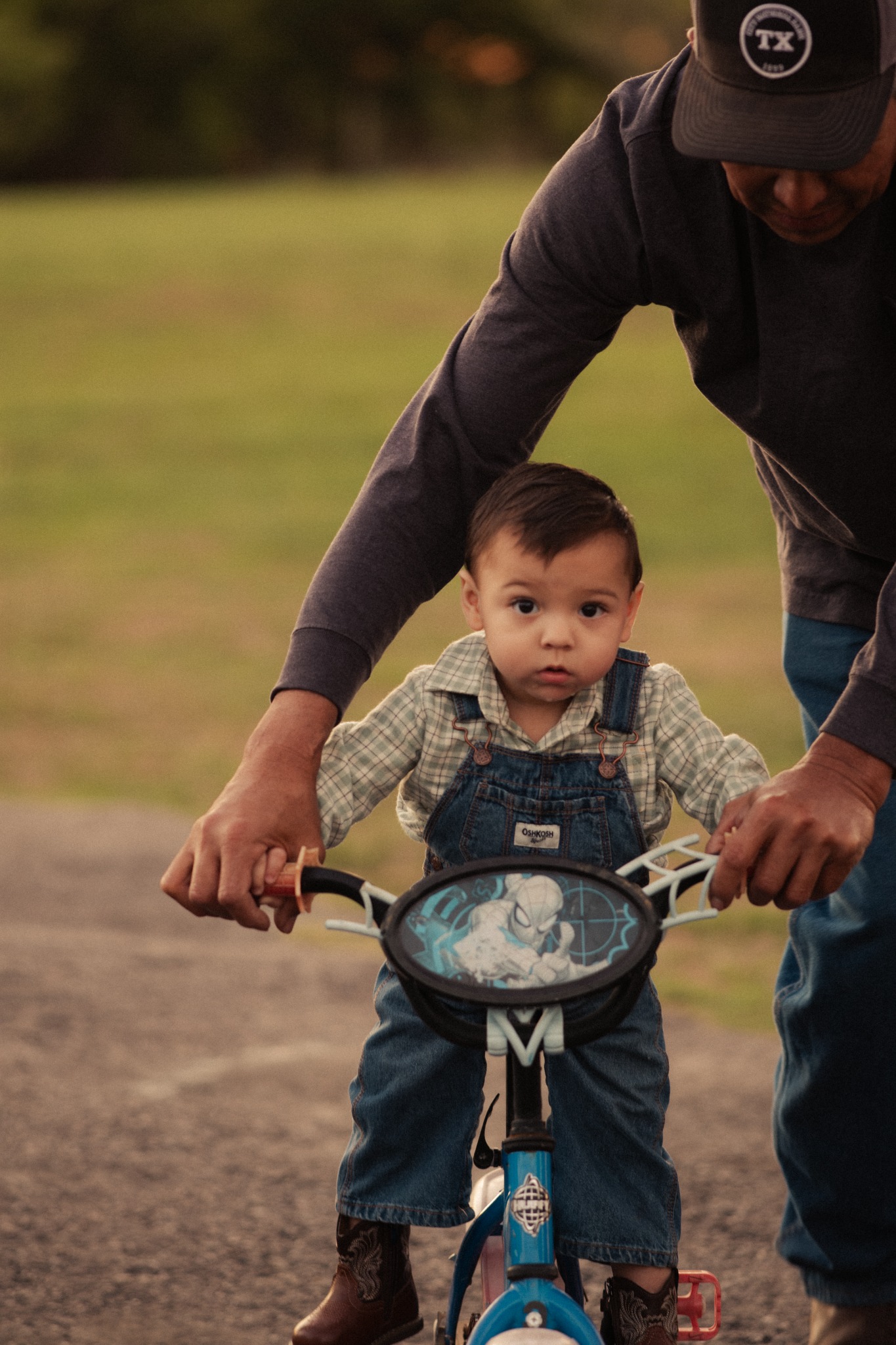A child on a small bicycle with an adult steadying the handlebars outdoors