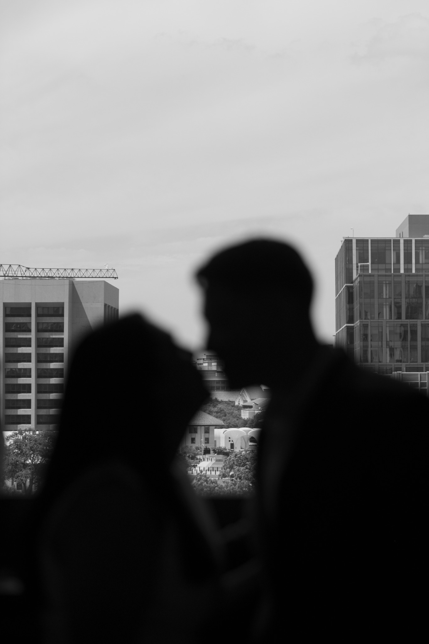 Soft silhouettes of a couple leaning toward a kiss against a city backdrop, in black and white