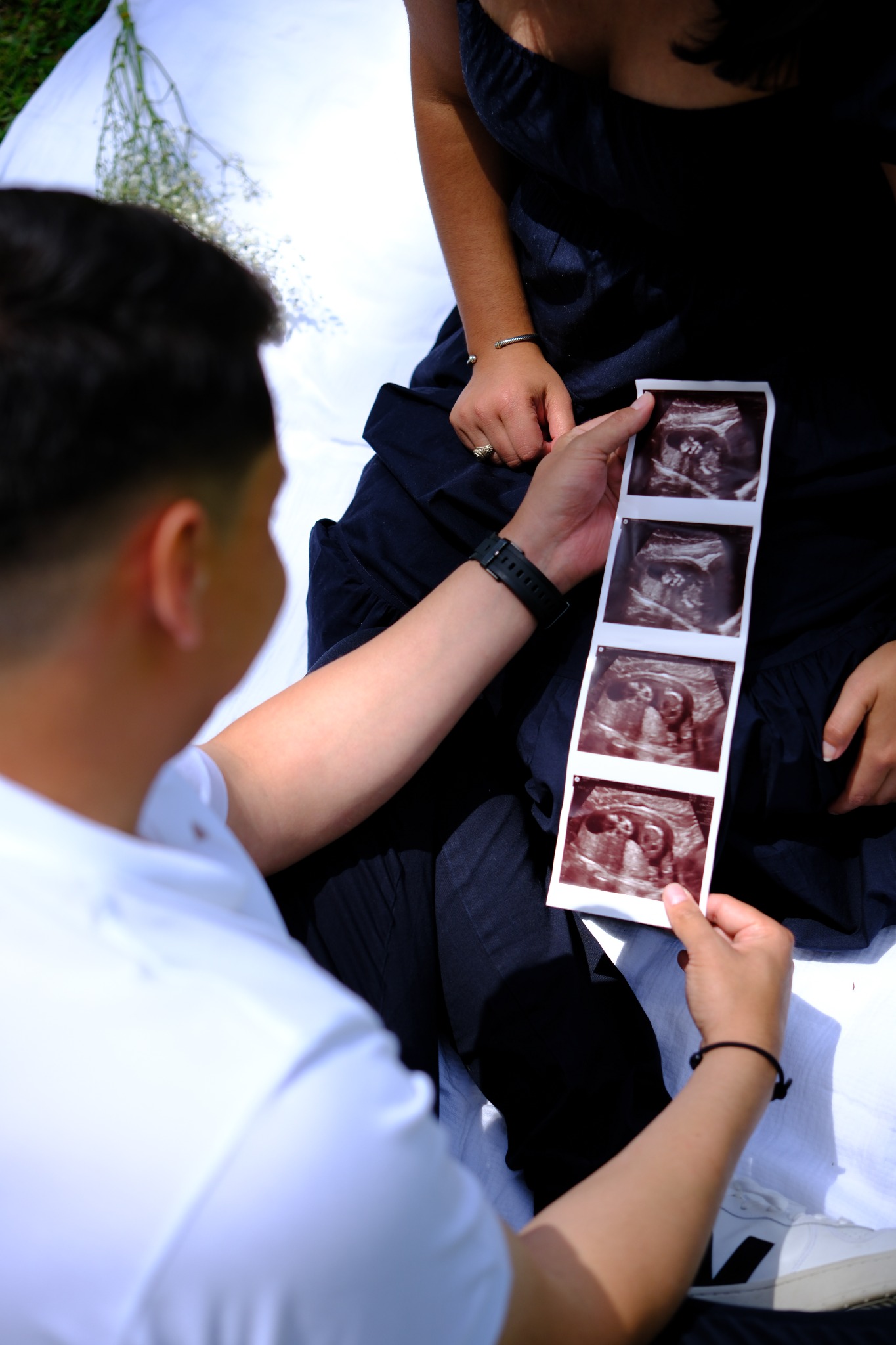 A couple seated together on a blanket looking at a strip of ultrasound photographs