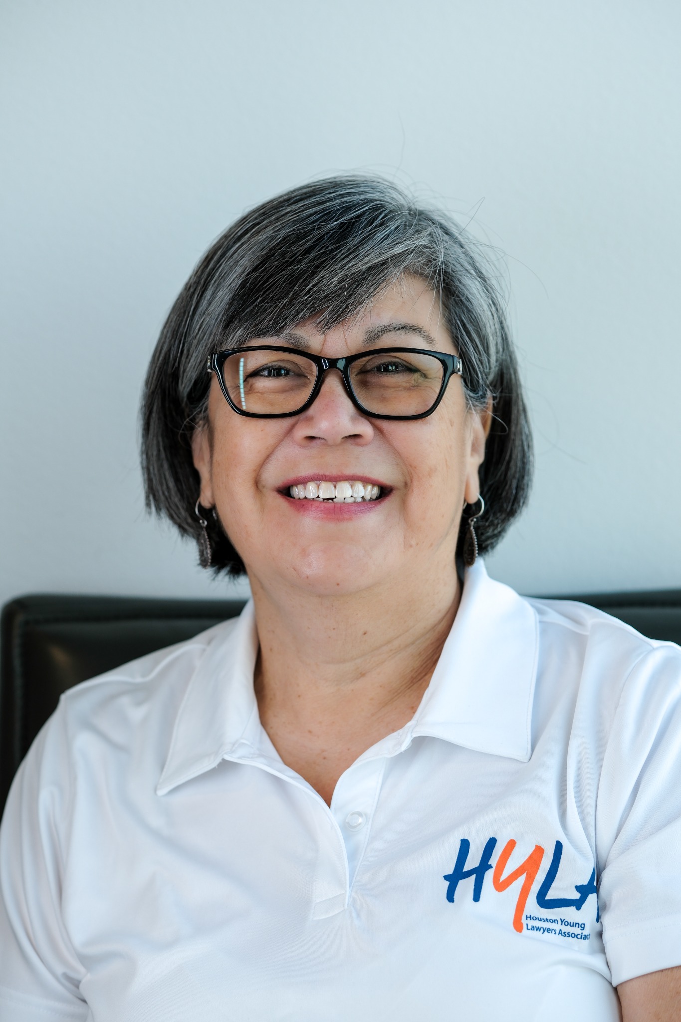A smiling woman with short gray hair and black glasses wearing a white embroidered polo shirt