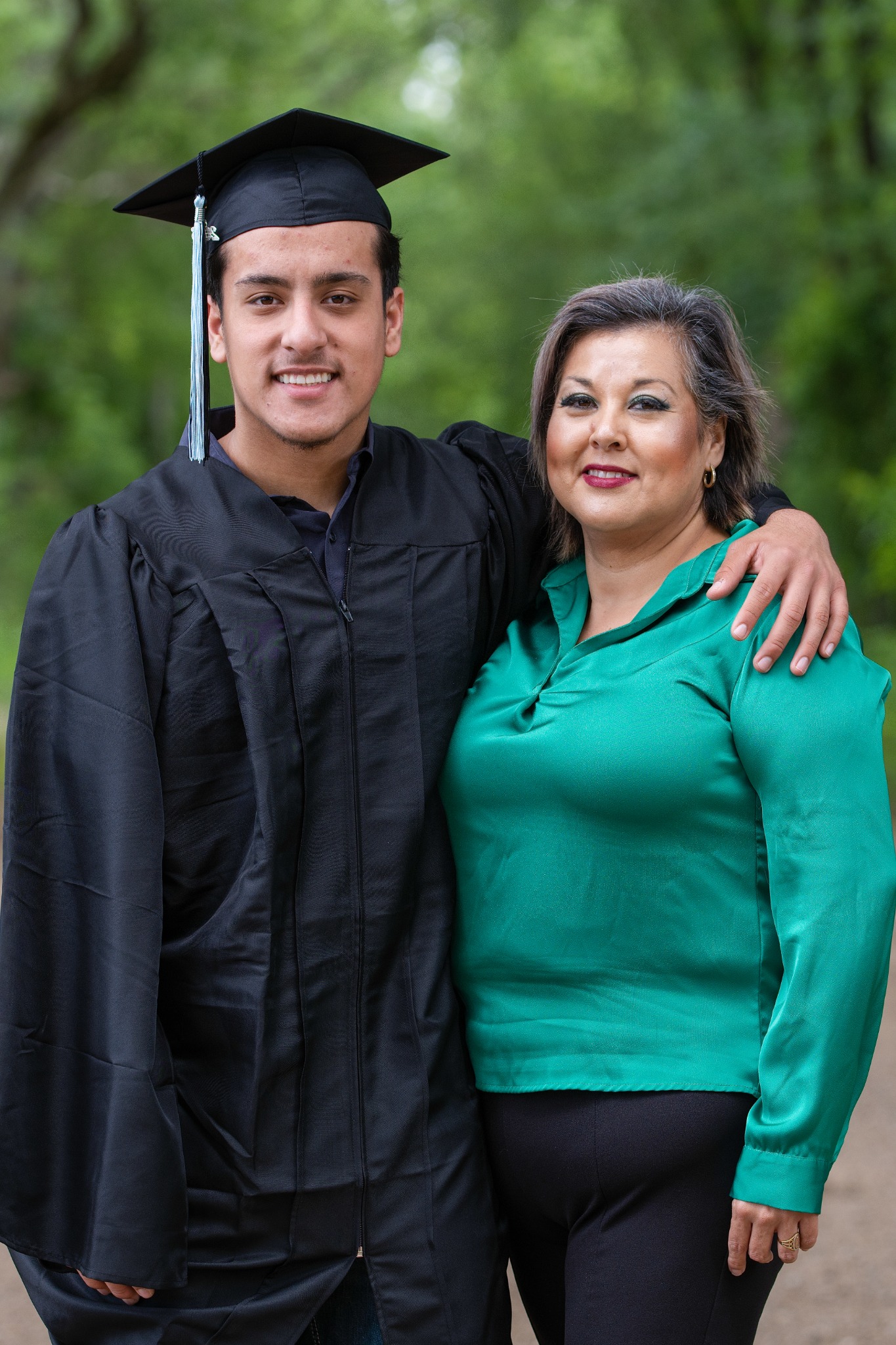 A graduate in a black cap and gown standing with an arm around a woman in a green blouse