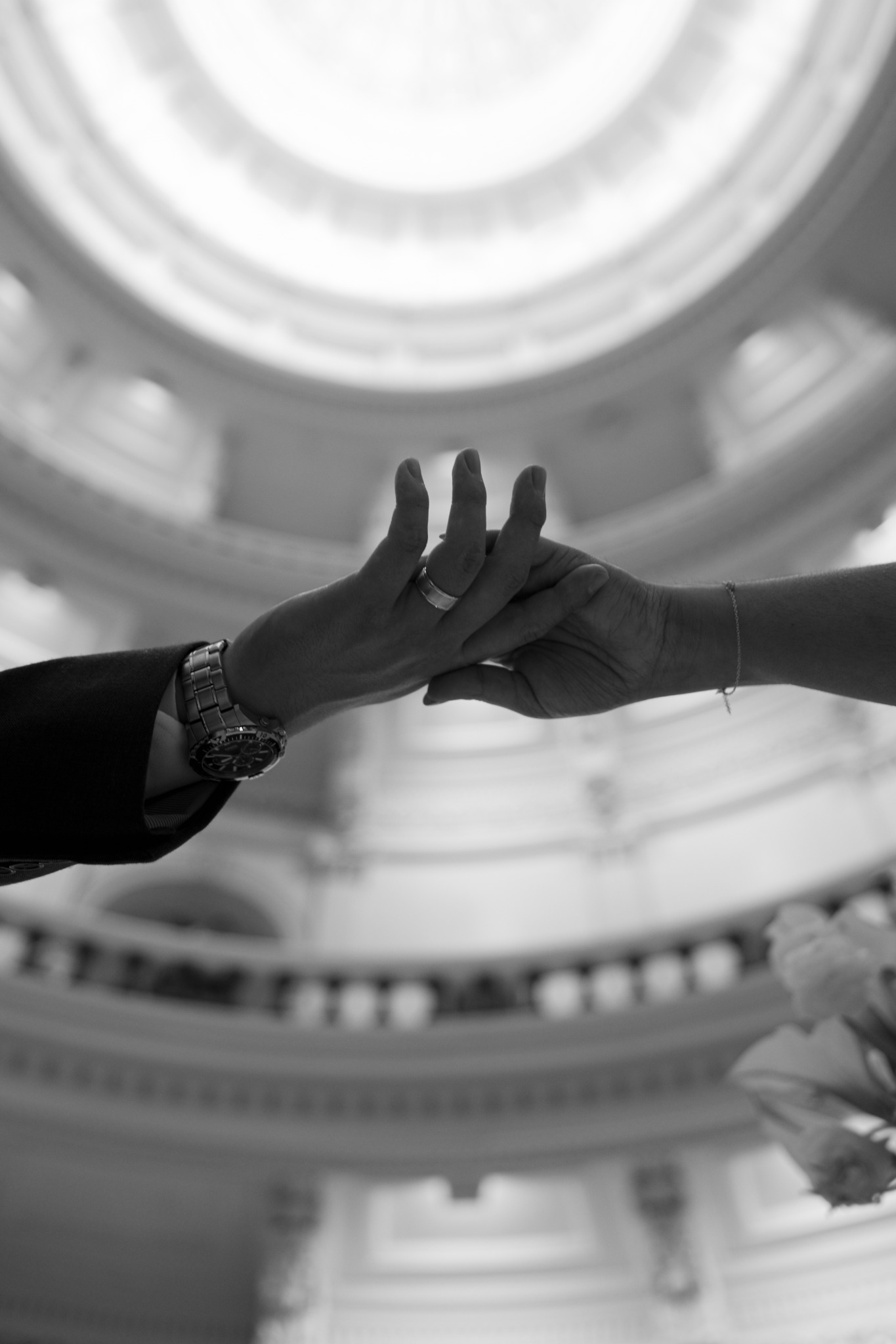 Two hands joined beneath a softly blurred domed ceiling, photographed in black and white