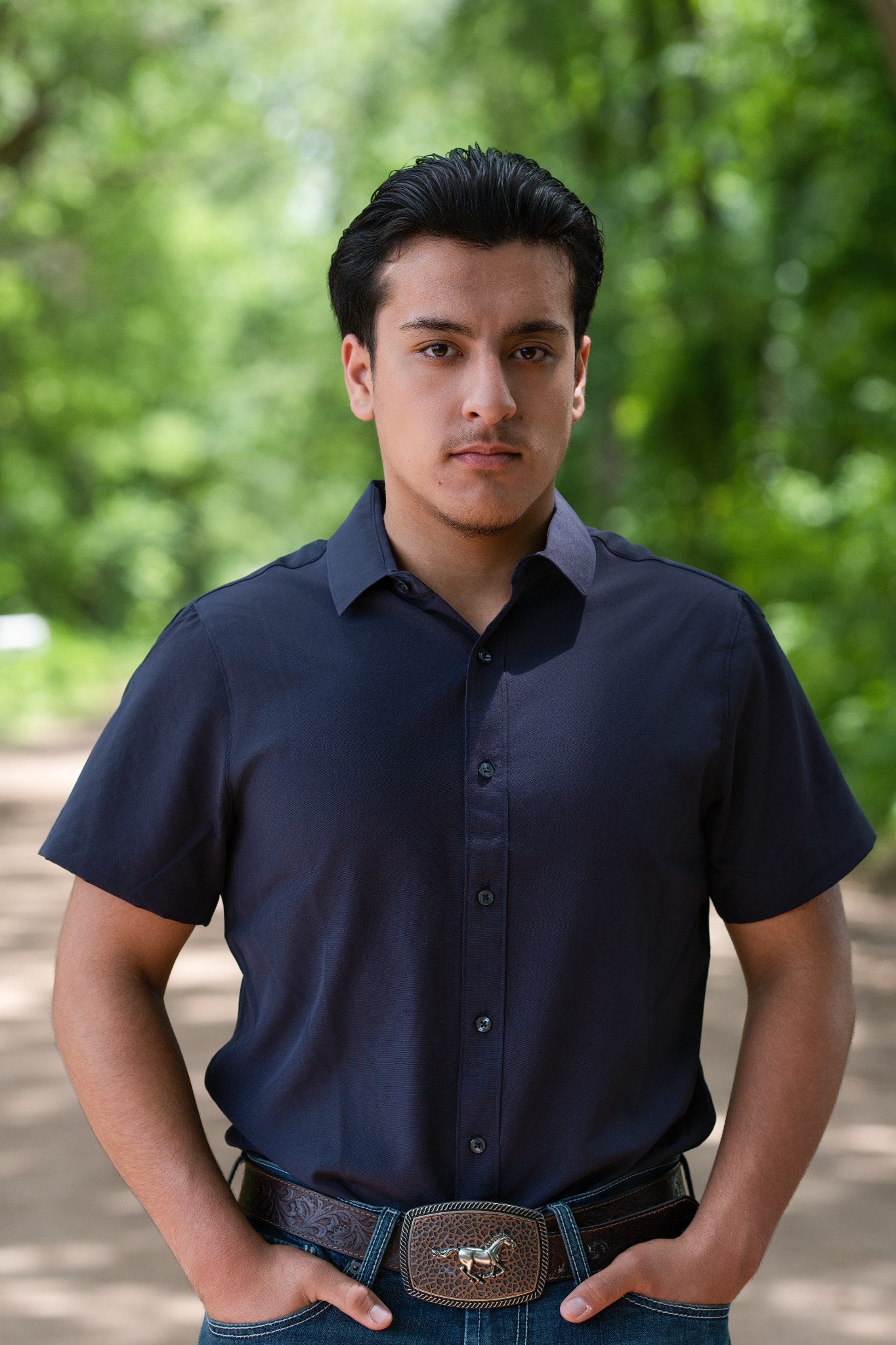 A young man in a navy short-sleeved shirt and jeans standing on a shaded path