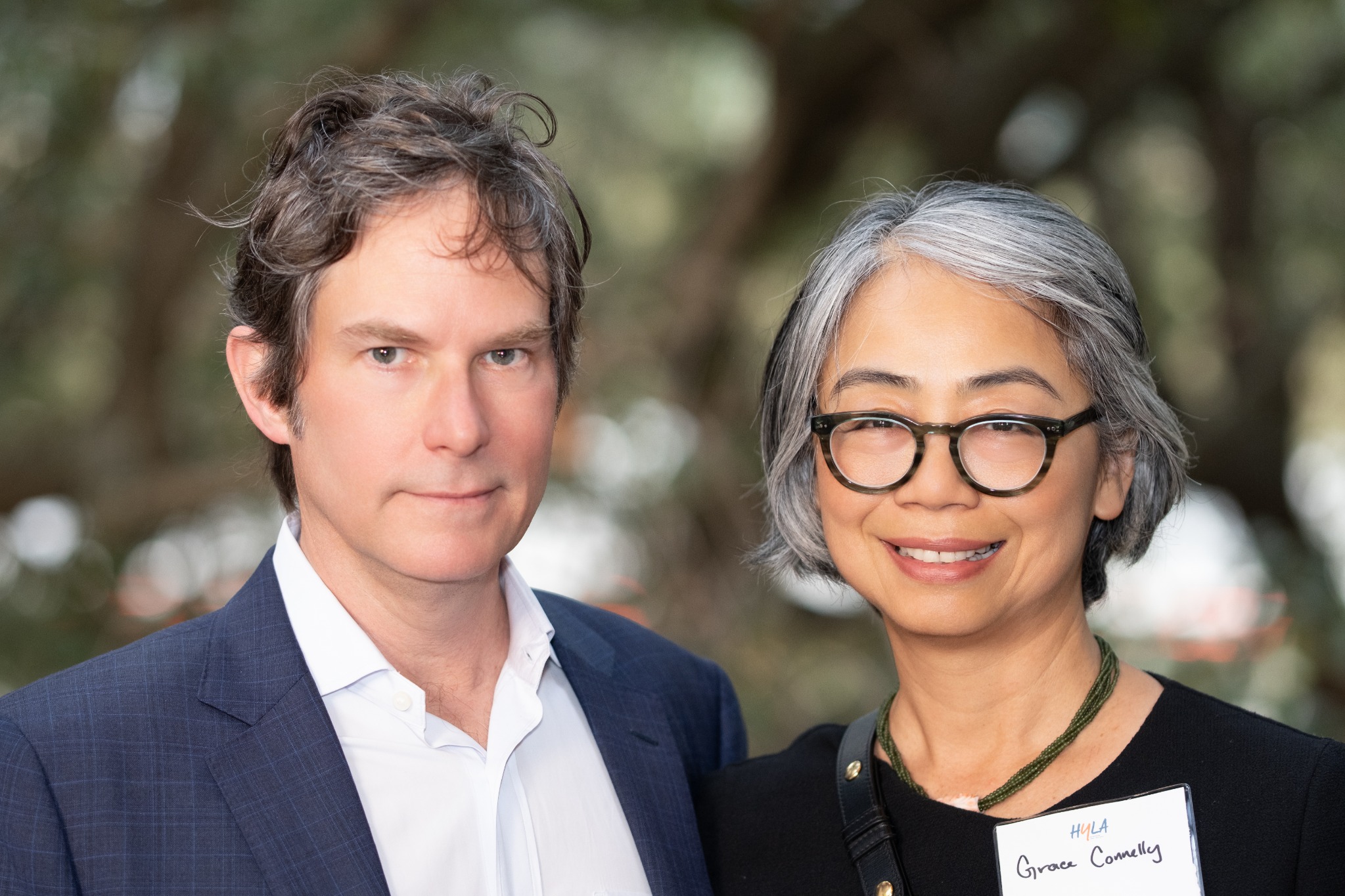 Two adults posing together outdoors, one in a navy jacket and one wearing glasses and an event badge
