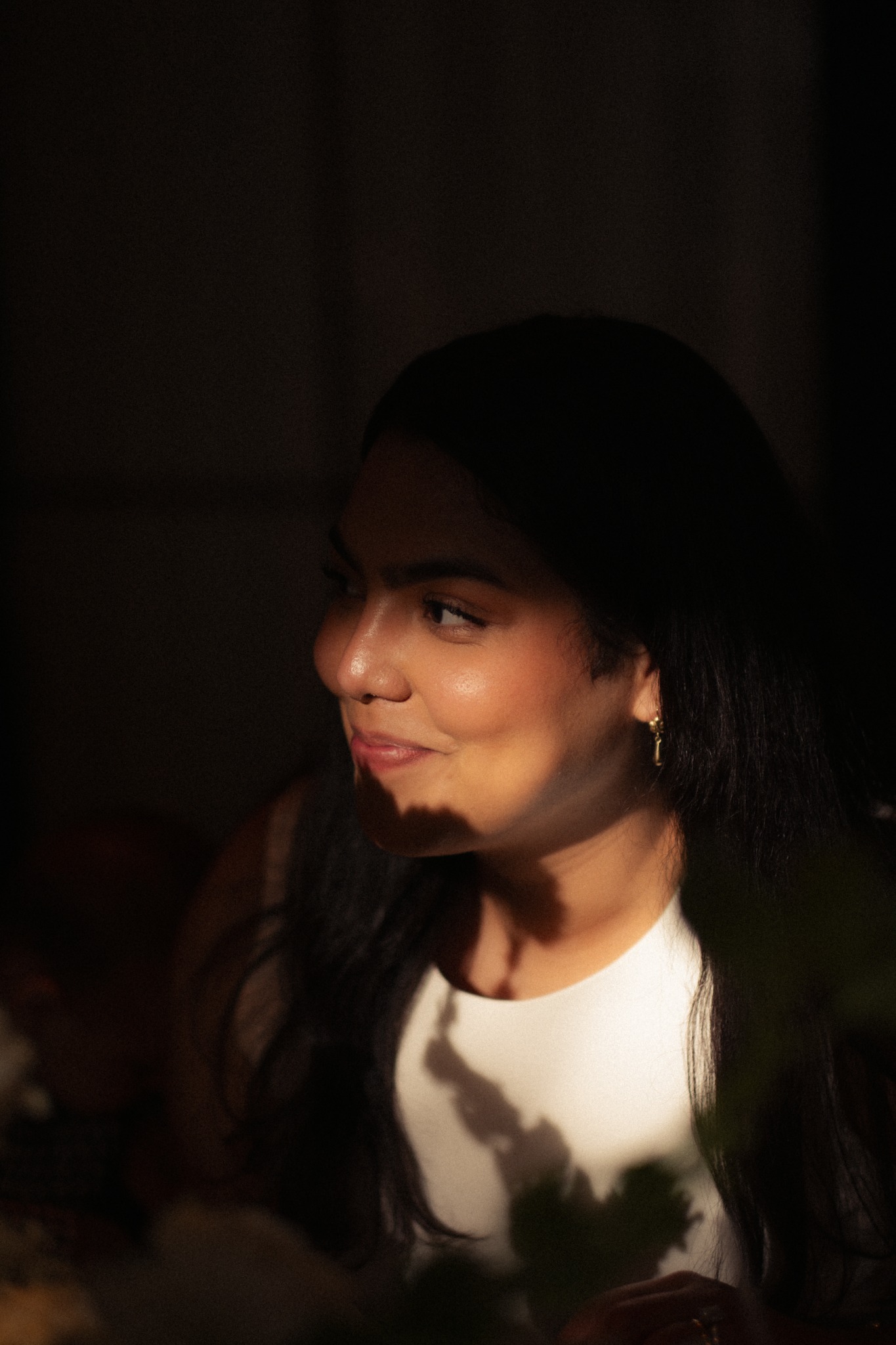 A close-up portrait of a woman with long dark hair, her face lit by a narrow patch of warm light