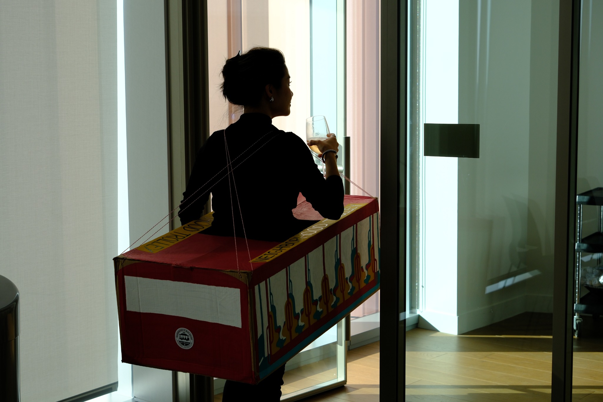 A guest wearing a red trolley costume holds a glass beside a sunlit doorway