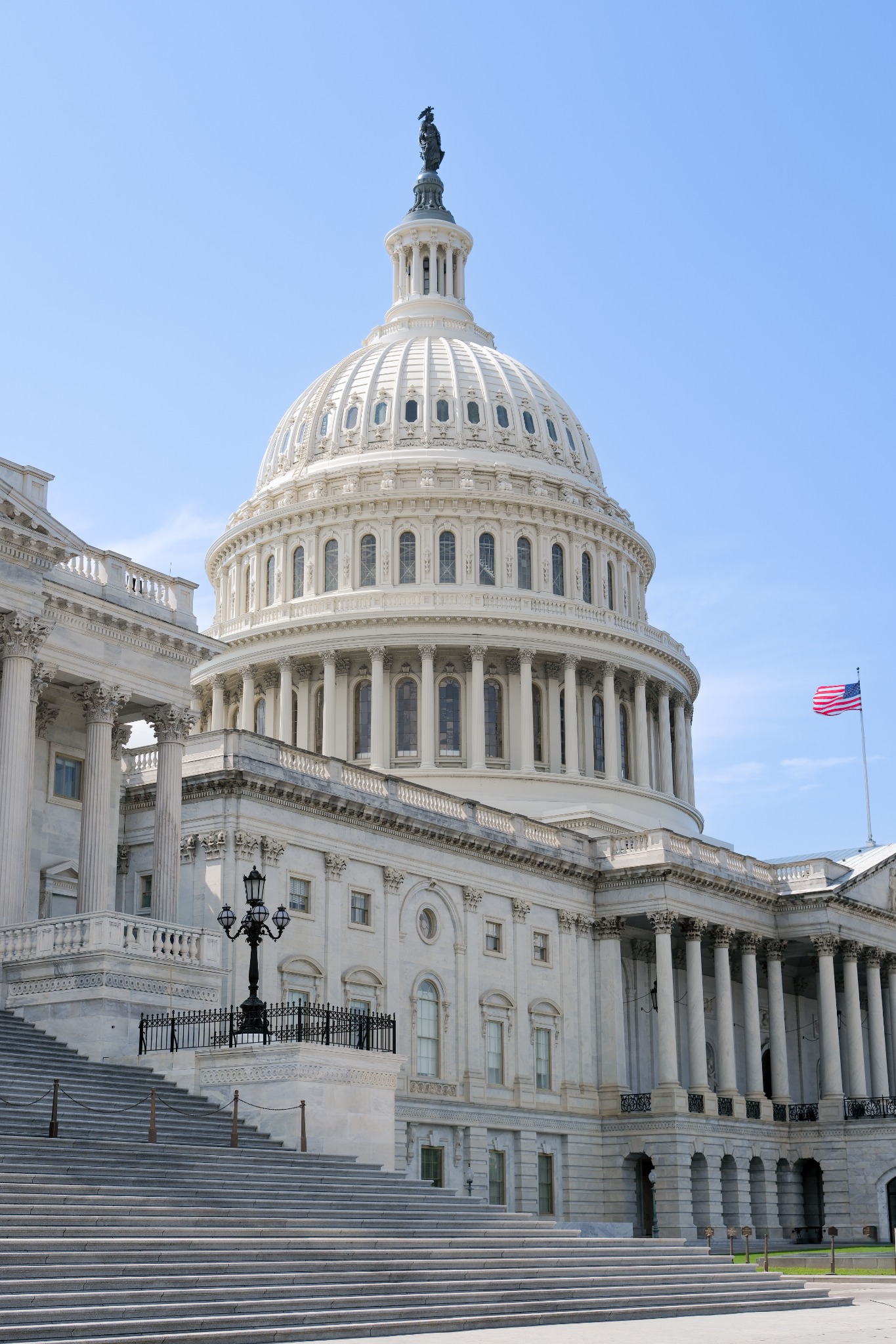 The white dome and broad steps of the United States Capitol beneath a clear blue sky