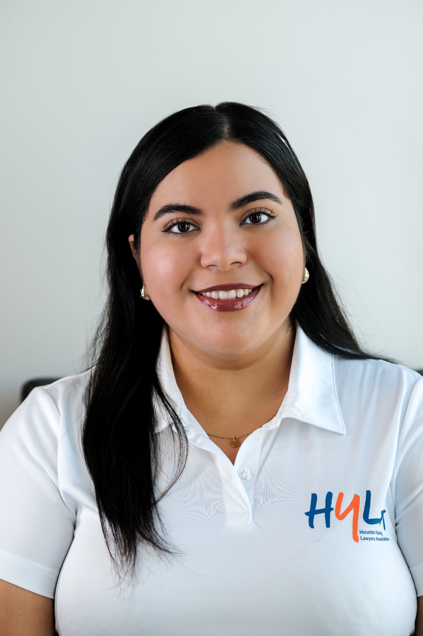 A smiling woman with long dark hair wearing a white embroidered polo shirt
