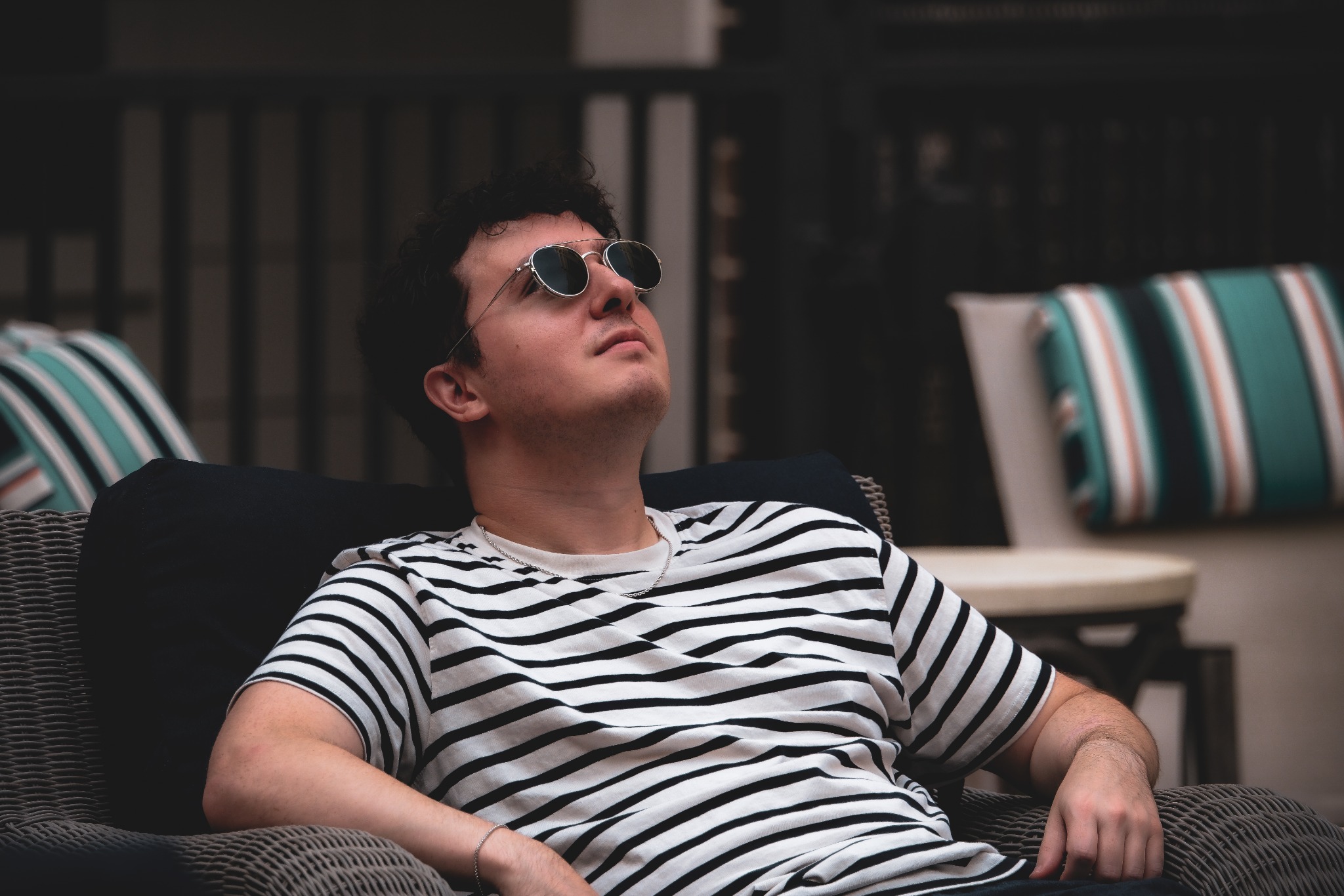 A man wearing sunglasses and a striped shirt reclines in a wicker chair